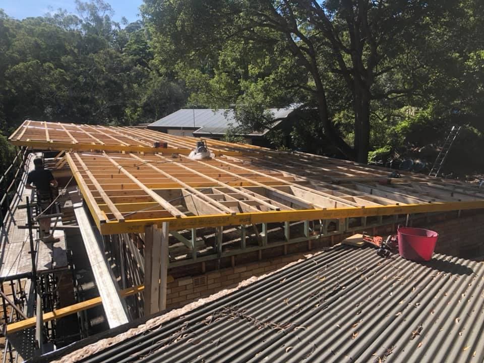 Carpenter setting out roof framing on a new extension, rafters and battens laid over the brickwork with scaffolding in place