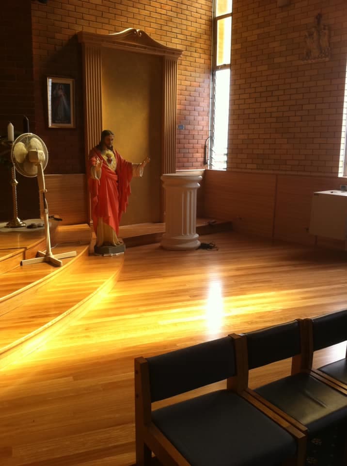 Church sanctuary with a new hardwood floor and a curved timber-edged altar platform, lit by afternoon light through stained glass
