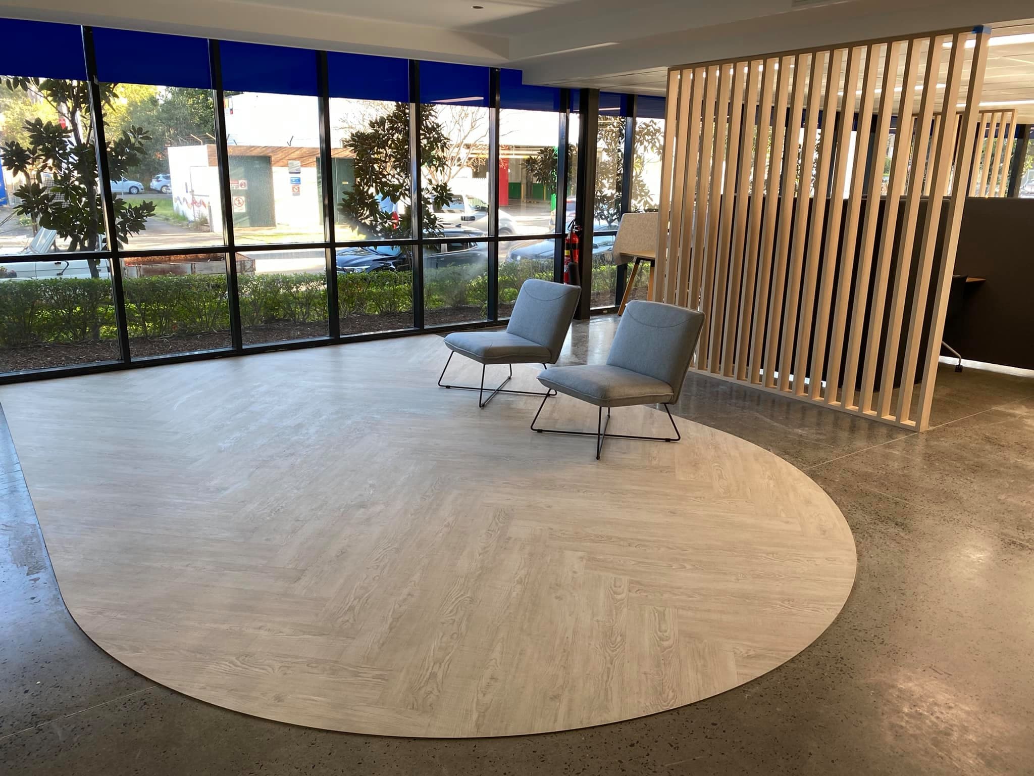 Office reception with a floor-to-ceiling vertical timber batten screen and a curved vinyl plank inlay set into polished concrete