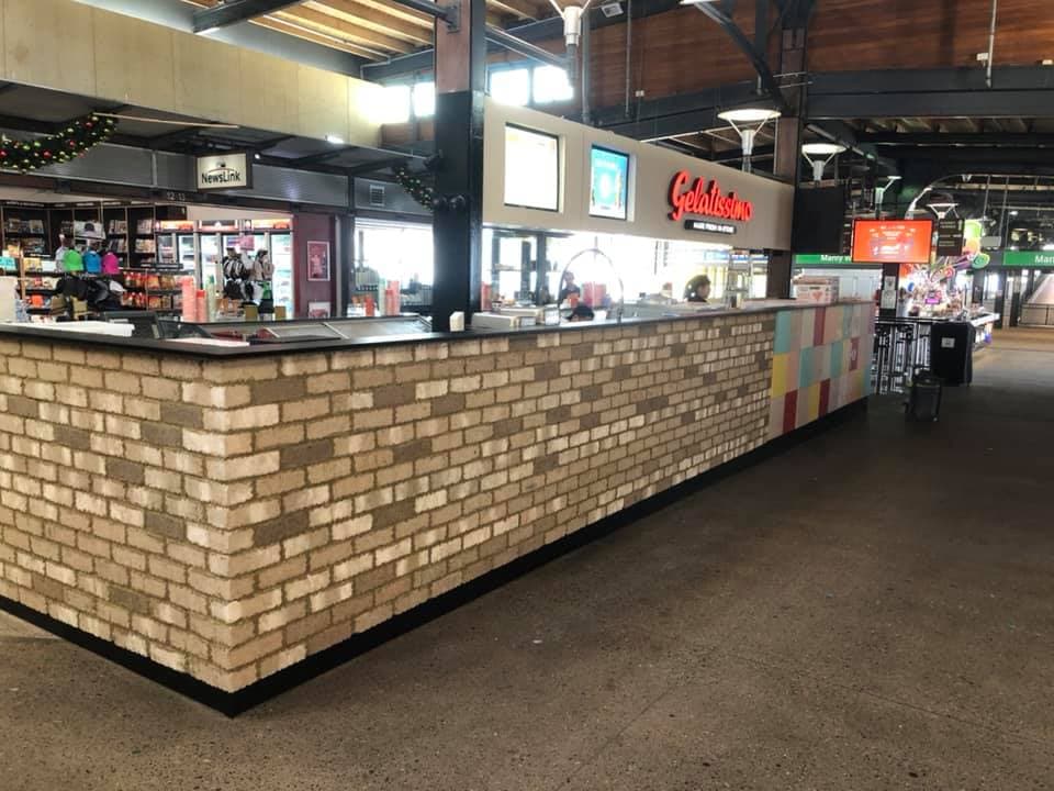Brick-clad servery counter with black stone benchtop and a tiled return, on a station concourse