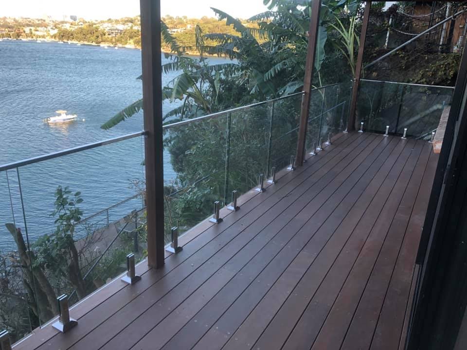 Hardwood deck with frameless glass balustrade on stainless spigots, cantilevered over a bushland slope above the water